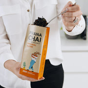 Person holding a Prana Chai box with a spoonful of black chai spice.