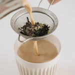 Person pouring a Prana Chai into a glass with a tea strainer